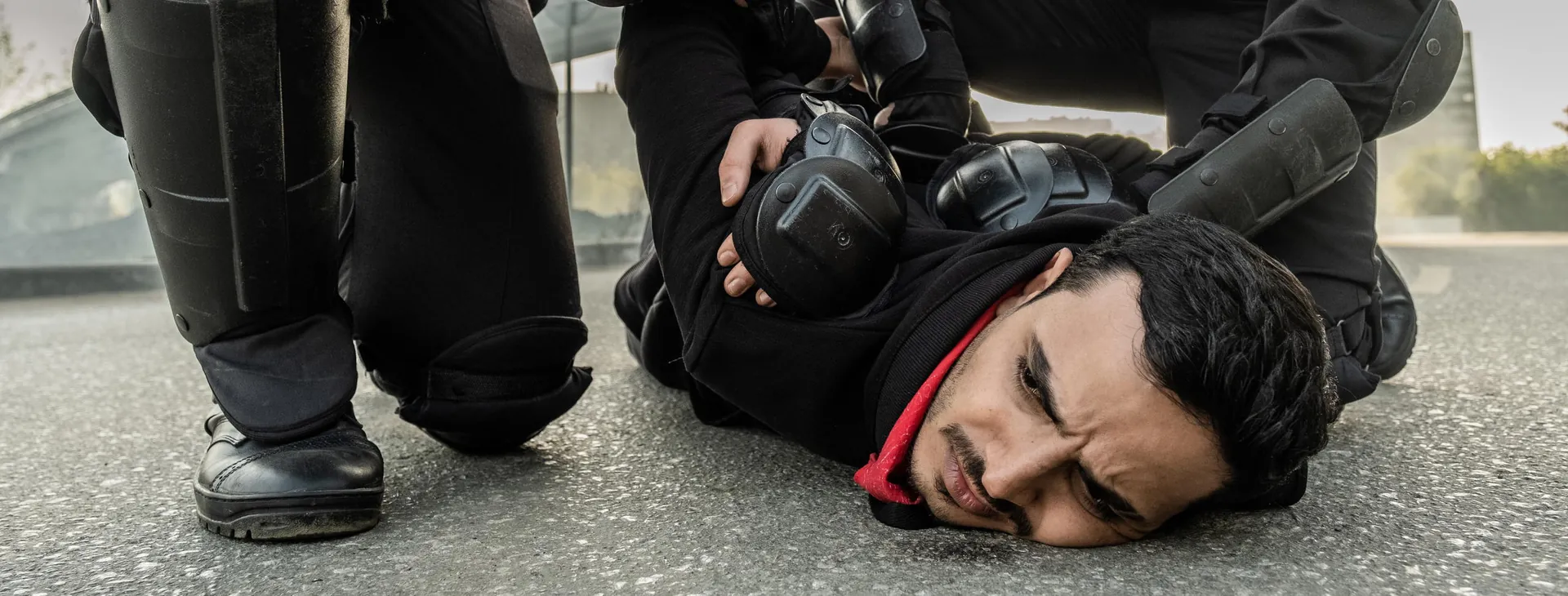 Officers in riot gear restraining a man on the ground